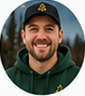 Portrait of a smiling light-skinned adult man in a dark baseball cap and green outerwear.
