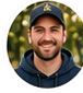 Circular portrait of a smiling man wearing a dark baseball cap and dark jacket.